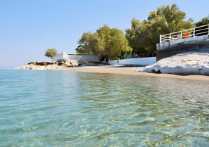 A beach with clear water, a white building, and trees.