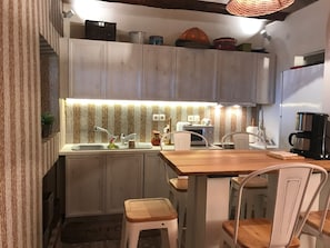 Une cuisine de taille réduite avec des meubles blancs, un plan de travail en bois, un évier, un four à micro-ondes et une machine à café.