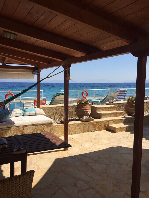 A covered outdoor area with a view of the sea, stone steps, lounge chairs, and a hammock.
