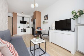 Ein modernes Wohnzimmer mit einer Couch, einem Couchtisch, einem Fernseher und einer Küche im Hintergrund.