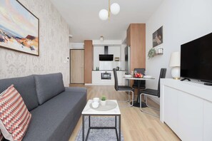 Ein modernes Wohnzimmer mit einem grauen Sofa, einem kleinen Tisch mit Pflanze und einem Fernseher auf einem weißen Schrank.