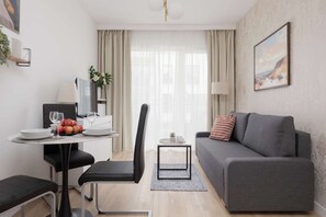Ein modernes Wohnzimmer mit einem grauen Sofa, einem Esstisch mit Stühlen, einem Fernseher und einem kleinen Beistelltisch mit einer Lampe.