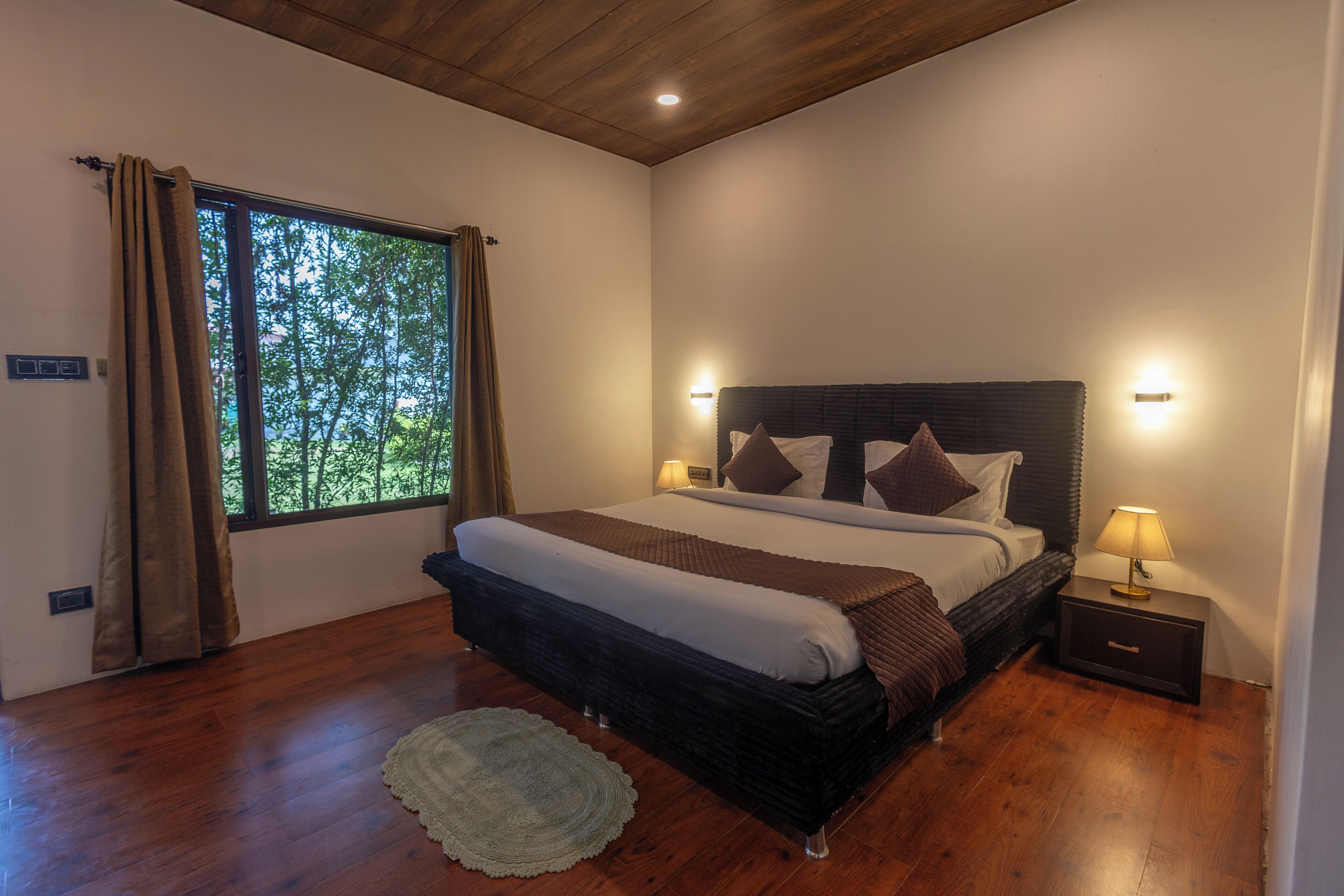 Un dormitorio con un ventanal grande, una cama con cabecera, lámparas de noche y suelo de madera.