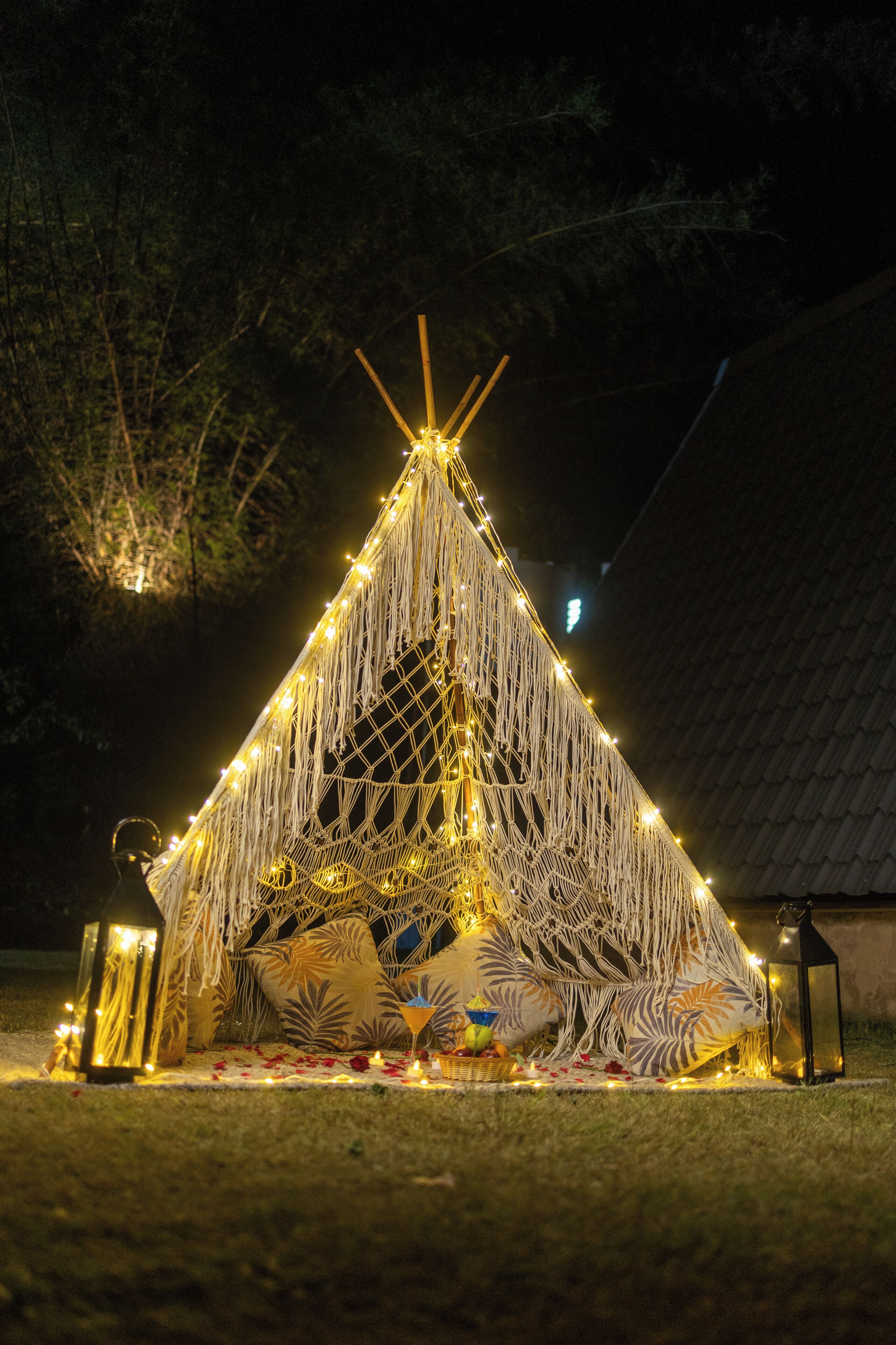 A geodesic dome structure with a conical roof, decorated with string lights and surrounded by a grassy area.