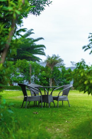 A set of wicker chairs arranged around a table in a grassy outdoor area with trees in the background. - The Arks Baagh Villas (Ramnagar)
