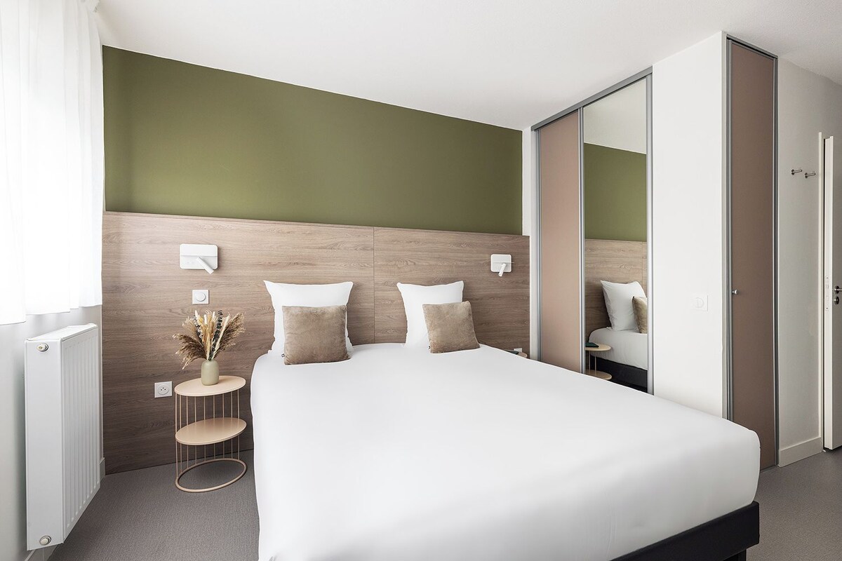 Ein modernes Hotelzimmer mit einem großen Bett, einem Nachttisch mit einer Vase und einem Schrank mit Spiegel.
