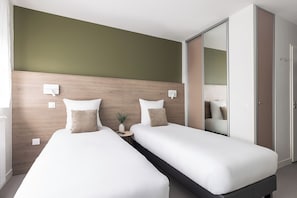 A hotel room with two single beds, a bedside table with a plant, a mirror, and a wardrobe. - Montempô Appart'hôtel Bordeaux Lac (Bordeaux)