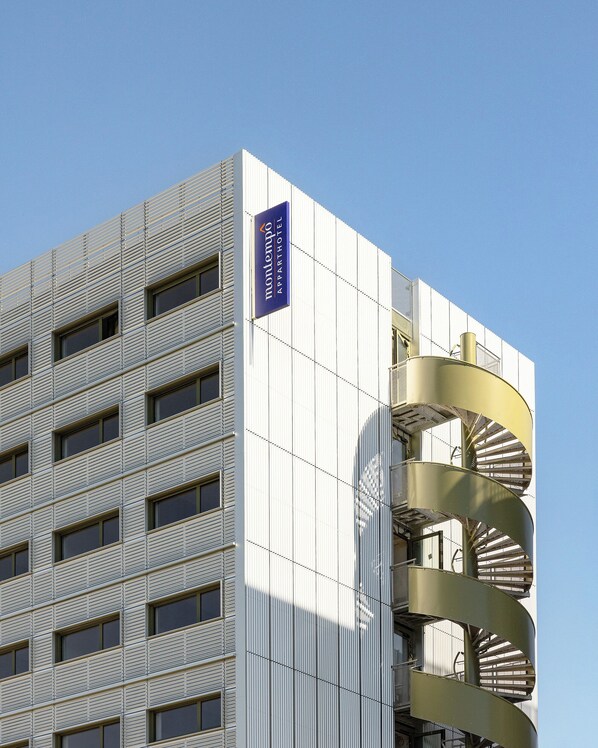 En modern byggnad med en skylt som visar namnet Montemulo Apartment Hotel. Byggnaden har en unik spiralformad trappa och flera fönster.