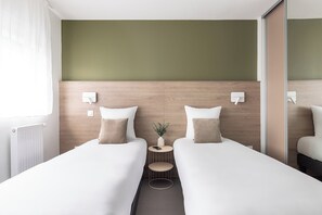 A hotel room with two single beds, a small round table, a vase with a plant, and a mirror on the wall. - Montempô Appart'hôtel Bordeaux Lac (Bordeaux)