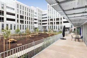 A modern building with multiple floors, outdoor seating area, and a garden with young trees.