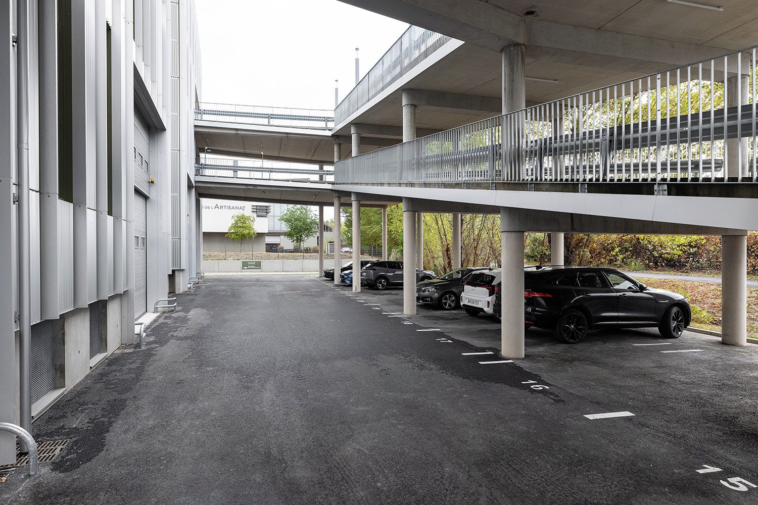 A parking area with multiple cars, a building with a sign, and a pedestrian bridge.