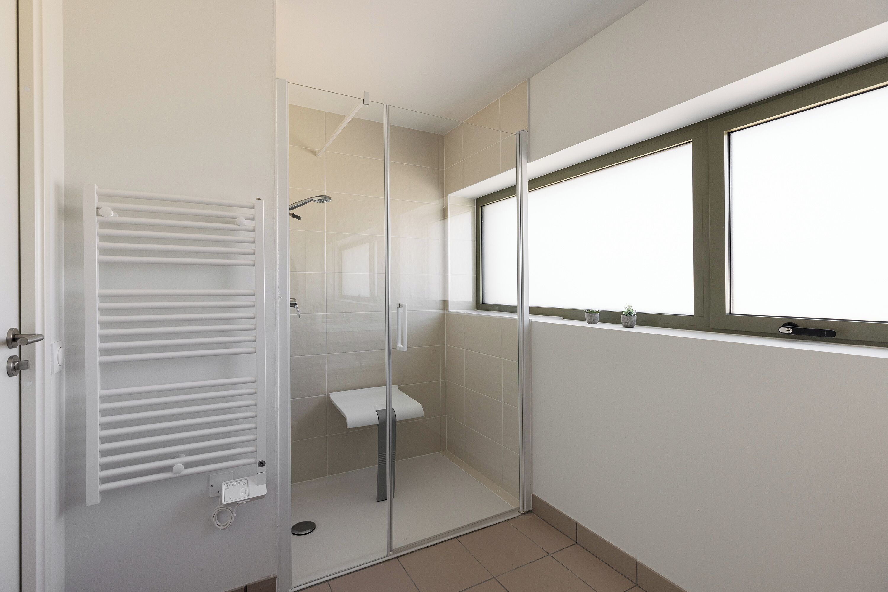 Un baño con cabina de ducha de vidrio, un perchero para toallas y una ventana.