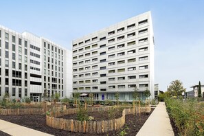 Een modern gebouw met meerdere verdiepingen, een centrale binnentuin met planten, en een heldere lucht.