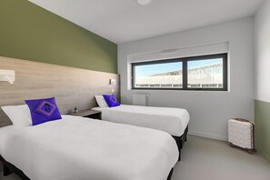 Ett hotellrum med två sängar, ett fönster med utsikt, en liten växt och en resväska.