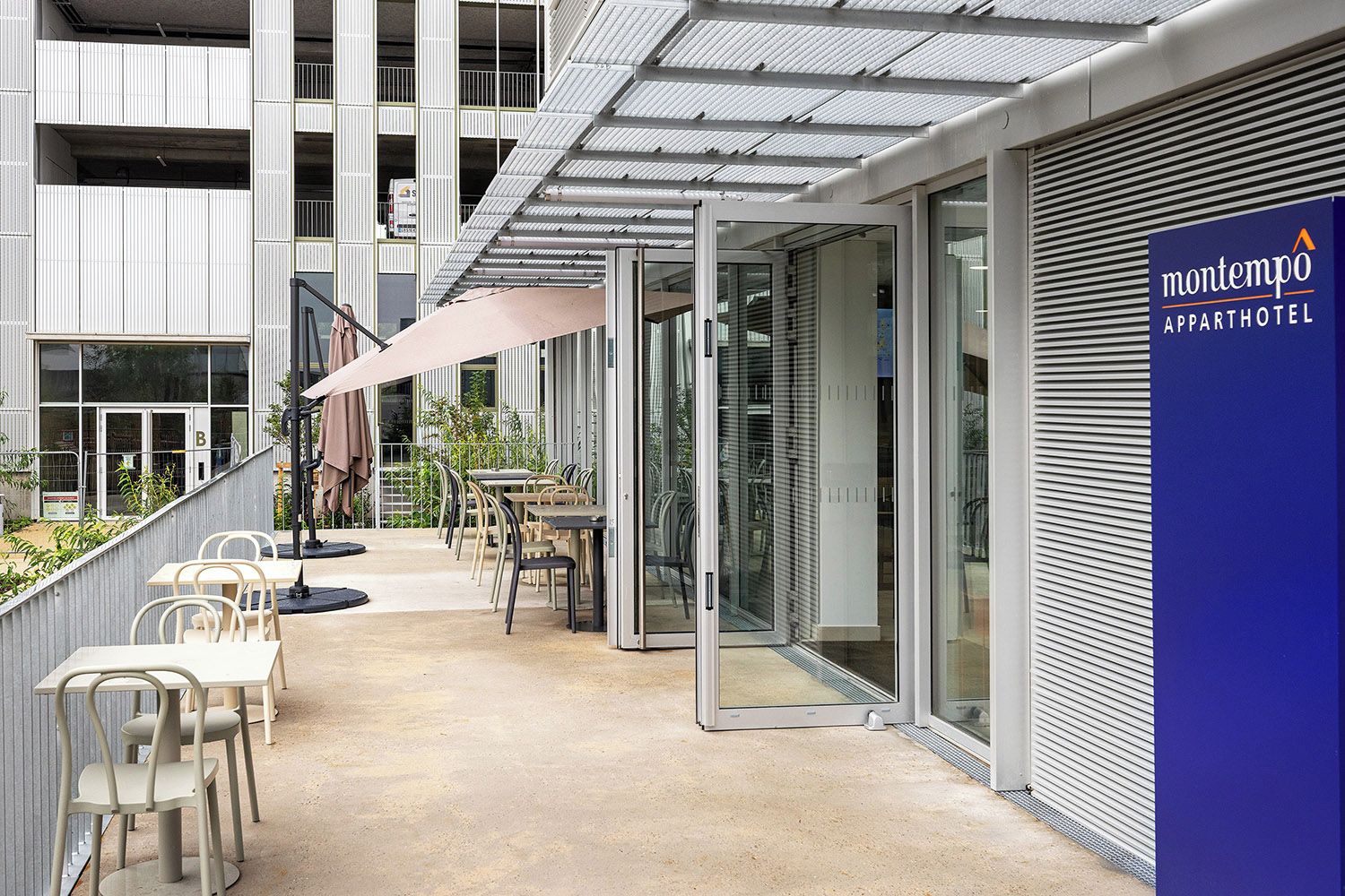 An outdoor seating area with tables and chairs, a covered patio, and a building with a sign for Montempo Apparthotel.