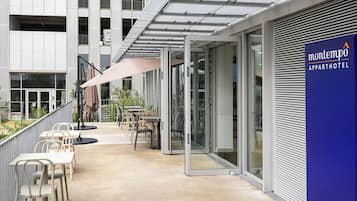 An outdoor seating area with tables and chairs, a covered patio, and a building with a sign for Montempo Apparthotel.