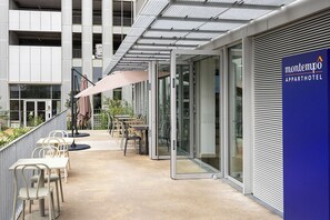 Ein Außenbereich mit Tischen und Stühlen, eine überdachte Terrasse und ein Gebäude mit der Beschilderung Montempo Apparthotel.