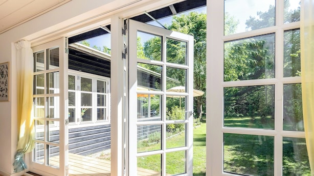 A room with a large open window, a wooden deck, and a view of a garden. - Cottage with forest idyll and peace by Arresø (Frederiksværk)