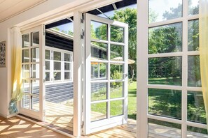Una habitación con un ventanal grande, una terraza de madera y vistas a un jardín.