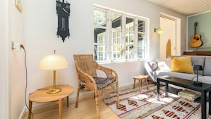 A living room with a wicker chair, a sofa, a coffee table, a lamp, and a guitar. - Cottage with forest idyll and peace by Arresø (Frederiksværk)