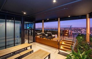 A modern rooftop terrace with a city view, wooden furniture, and a staircase leading to an upper level. - Stunning 2 Bedroom Retreat with Rooftop Pool! (Fortitude Valley)