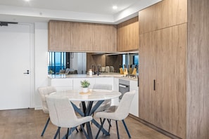 A modern kitchen with a central island, a dining area with a round table and chairs, and wooden cabinetry. - Stunning 2 Bedroom Retreat with Rooftop Pool! (Fortitude Valley)