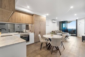 A modern kitchen with a dining area, a sofa, and a view of the sea. - Stunning 2 Bedroom Retreat with Rooftop Pool! (Fortitude Valley)