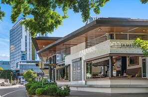 A modern building with a glass facade, a prominent 'James' sign, and a rooftop garden. - Stunning 2 Bedroom Retreat with Rooftop Pool! (Fortitude Valley)