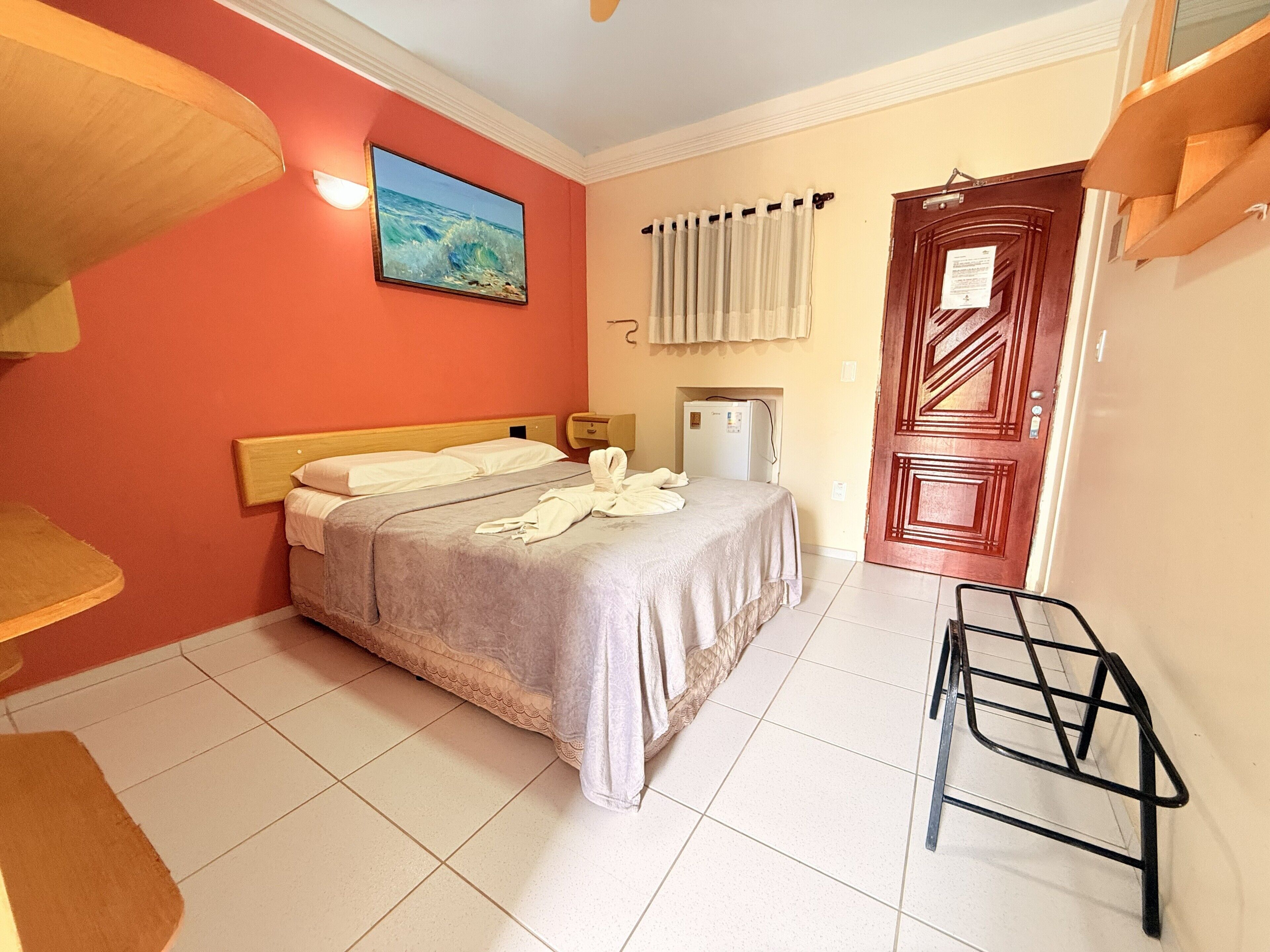 A hotel room with a bed, a refrigerator, a wooden door, and a window with curtains.