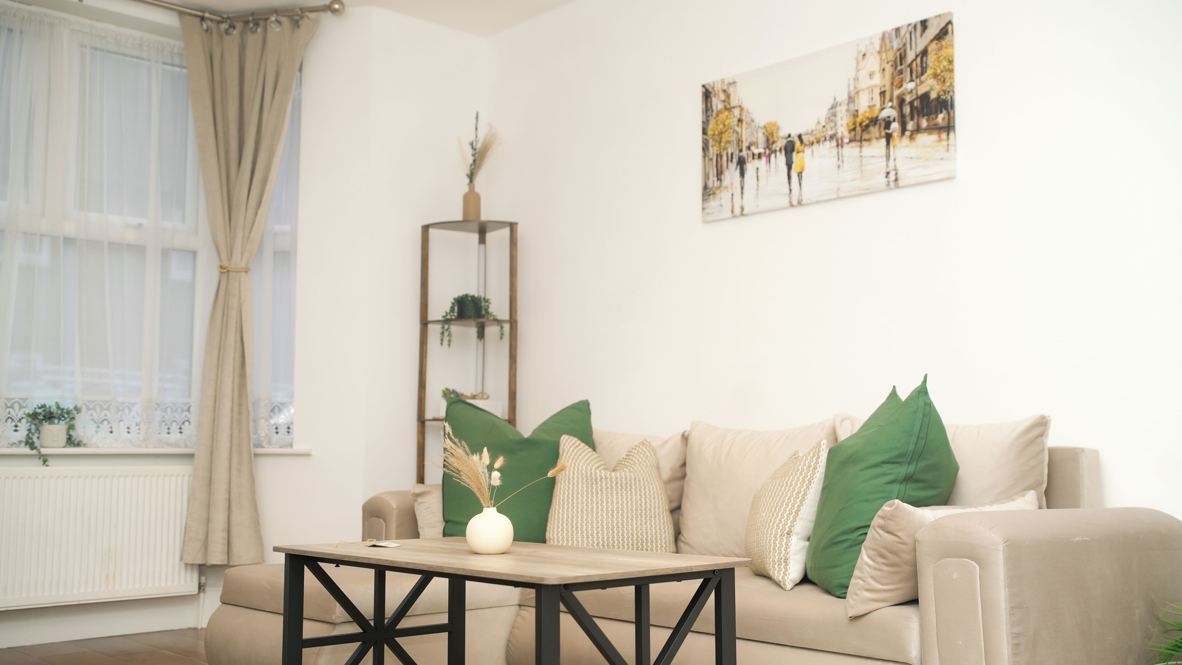 A living room with a beige sofa, a wooden coffee table, a tall plant stand, and a cityscape painting on the wall.