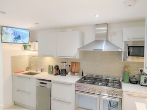 A modern kitchen with a gas stove, oven, dishwasher, and a flat-screen TV mounted on the wall. - Luxury 3BR Home. 20 Mins to London. Garden + Wi-Fi. Sleeps 8 (Gravesend)
