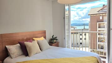 Una camera d'albergo con un letto, un comodino, una finestra vista edifici e uno specchio d'acqua.