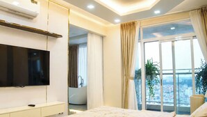 Een moderne slaapkamer met een groot bed, een televisie, een balkon met uitzicht op de stad, en een badkamer die door een open deur zichtbaar is.