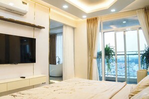 Ein modernes Schlafzimmer mit einem großen Bett, einem Fernseher, einem Balkon mit Blick auf die Stadt und einem durchgehenden Tür erkennbaren Badezimmer.