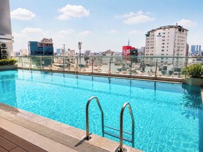 A rooftop pool with clear blue water, surrounded by a glass railing, overlooking a cityscape with various buildings. - The Crown Luxury 4BR Penthouse (Ho Chi Minh City)