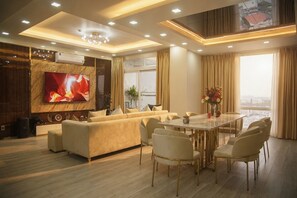 A modern living room with a sofa, dining table, chairs, a TV, and a large window. - The Crown Luxury 4BR Penthouse (Phu Nhuan)