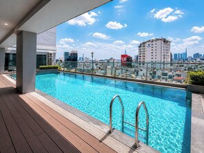 A rooftop swimming pool with a city view, metal railings, and a wooden deck. - The Crown Luxury 4BR Penthouse (Phu Nhuan)