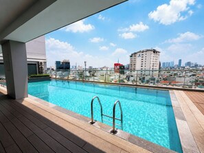 Una piscina en la azotea con vista a un paisaje urbano, barandillas de metal y cielo despejado.