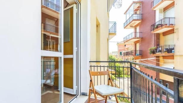 Un balcone con una sedia, un'uscita in vetro e vista sugli edifici vicini.