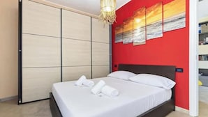 Una camera da letto con un letto, un armadio e una parete rossa decorata con opere d'arte.