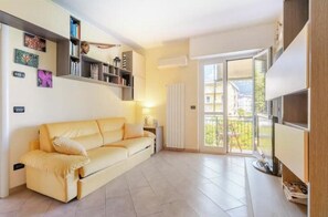 A modern living room with a sofa, a bookshelf, and a sliding glass door to a balcony. - Hostdomus - Apnea House (Finale Ligure)