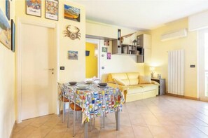 A dining area with a table set for four, a yellow sofa, a bookshelf, and a white radiator. - Hostdomus - Apnea House (Finale Ligure)