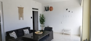 A modern living room with a sofa, a dining table, a potted plant, and a hanging light fixture.
