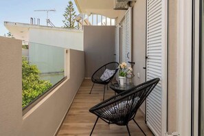 A balcony with two black chairs, a small table with a vase of flowers, and a glass railing overlooking greenery. - Villy Suites II - Zante Lux Suite Near the Beach (Argassi)