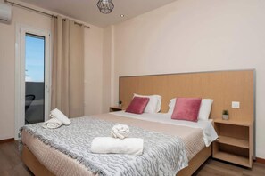 A bedroom with a bed, pillows, a bedside table, a nightstand, a window with curtains, and a door. - Villy Suites II - Zante Lux Suite Near the Beach (Argassi)