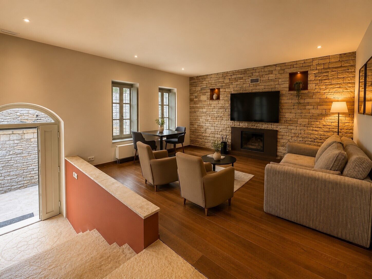 Una sala de estar moderna con chimenea, un televisor de pantalla plana montado en una pared de piedra y una zona de estar con sofá y sillones.