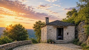 A stone cottage with a circular stone patio, a chimney, and a door leading to a room. - Monopatia Resort (Zagori)