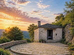 Una cabaña de piedra con un patio circular de piedra, una chimenea y una puerta que da a una habitación.