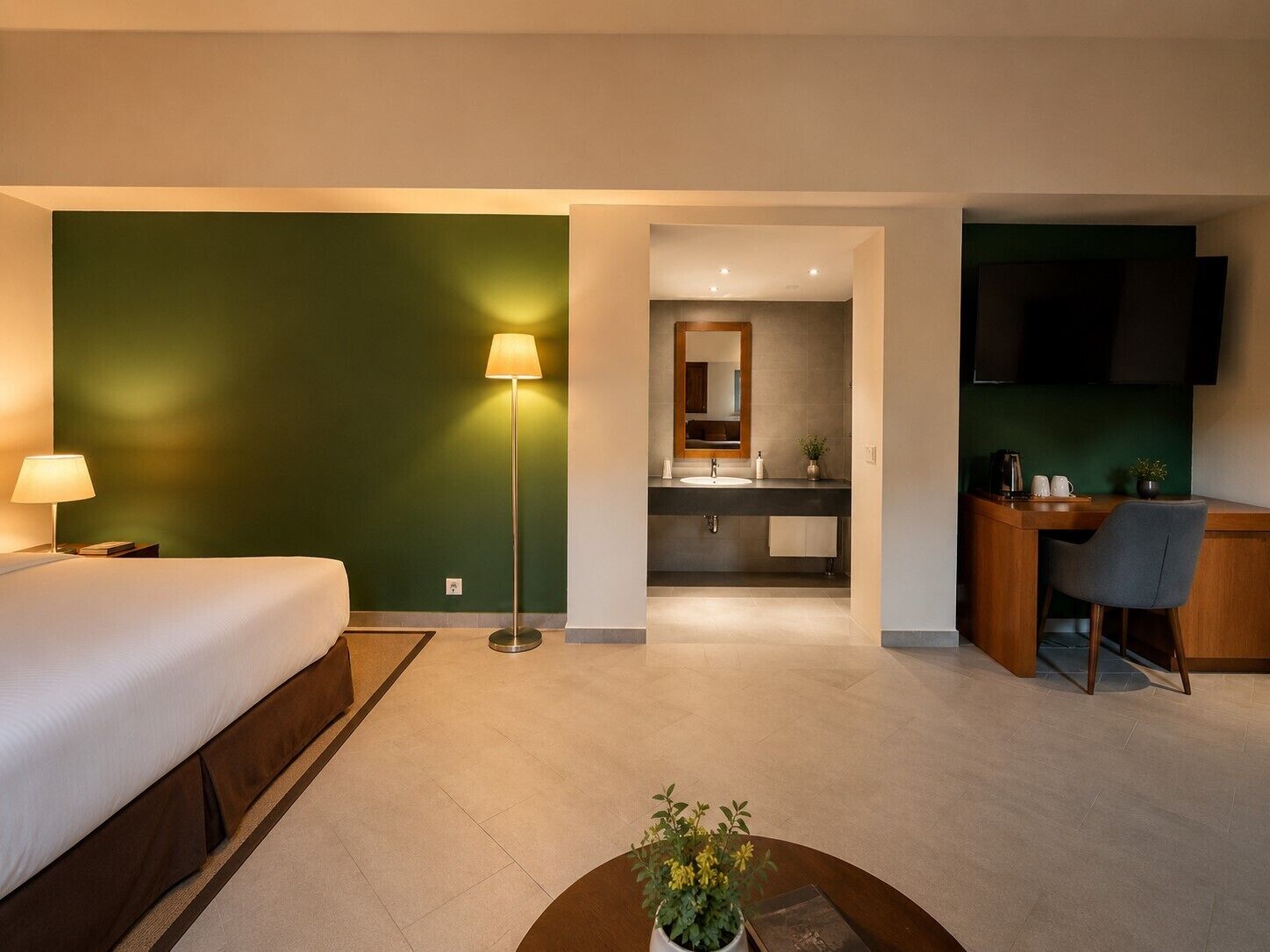 A hotel room with a bed, desk, chair, lamp, and a small plant.
