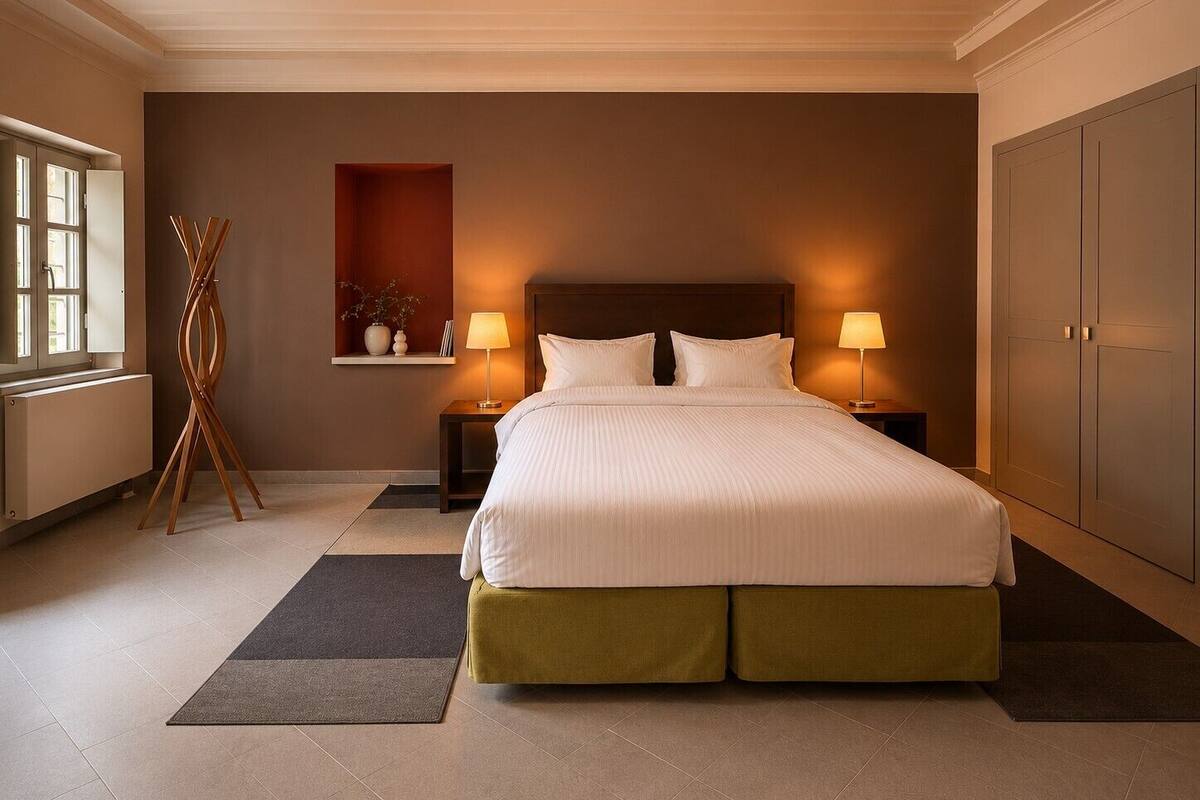 Una habitación de hotel con una cama grande, dos mesitas de noche con lámparas, un radiador, una lámpara de pie de madera y un armario.
